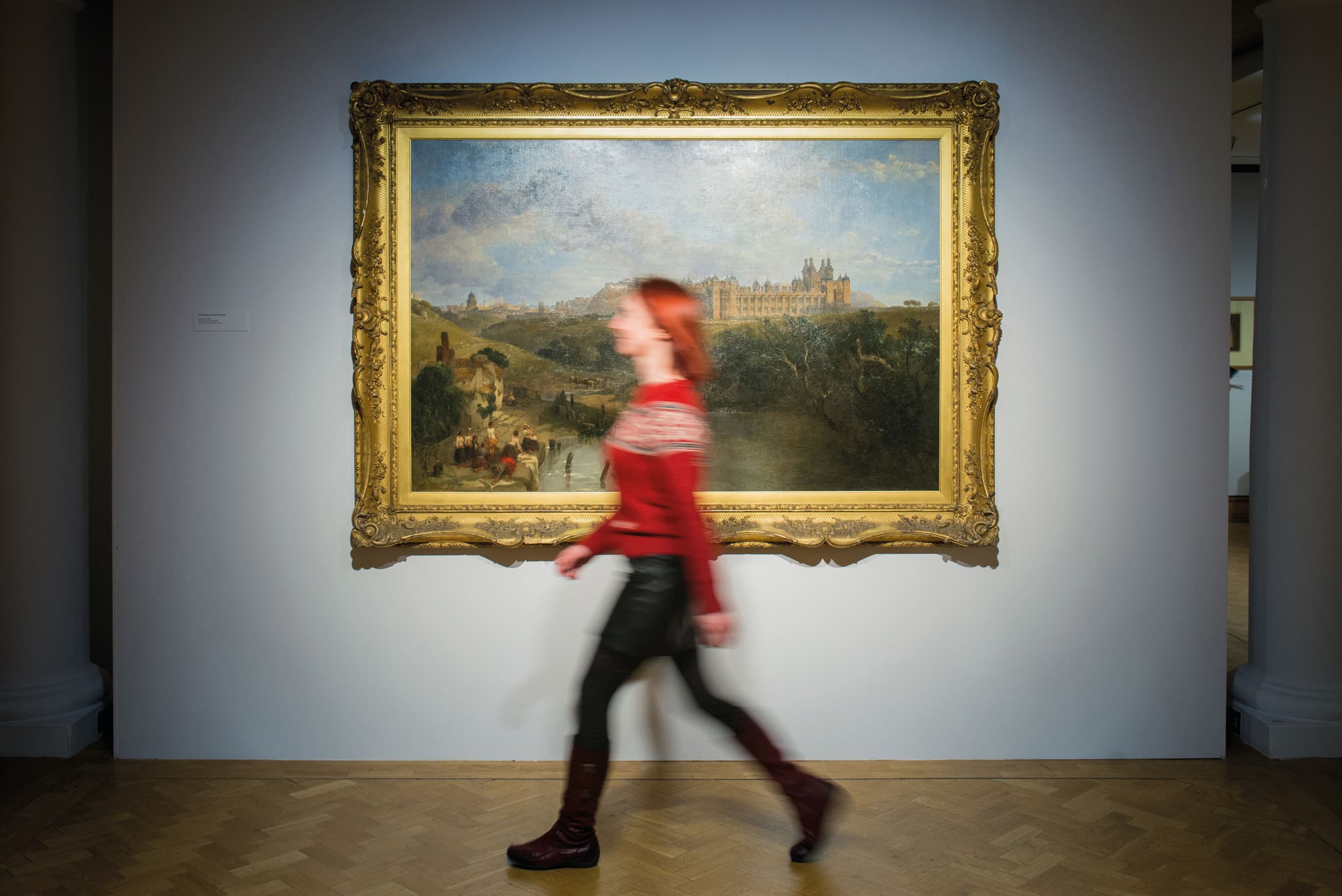 A woman walks past a colorful painting displayed on a wall in an art gallery.