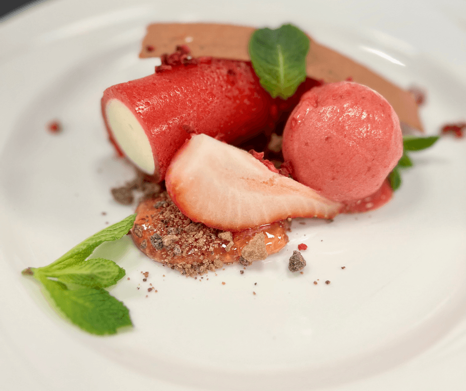 A plate featuring a fresh strawberry, a scoop of ice cream, and a piece of chocolate arranged artfully.