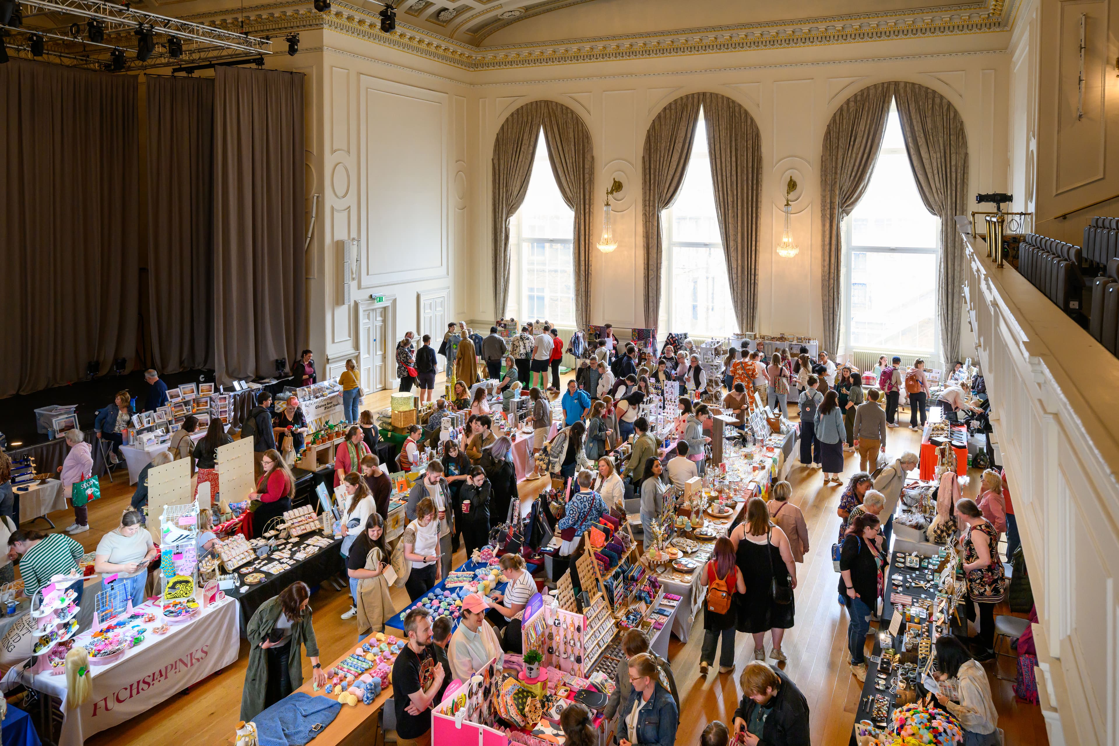 A large gathering of people visiting a Craft fair in the Music room, interacting and participating in various discussions about gifts and company items.