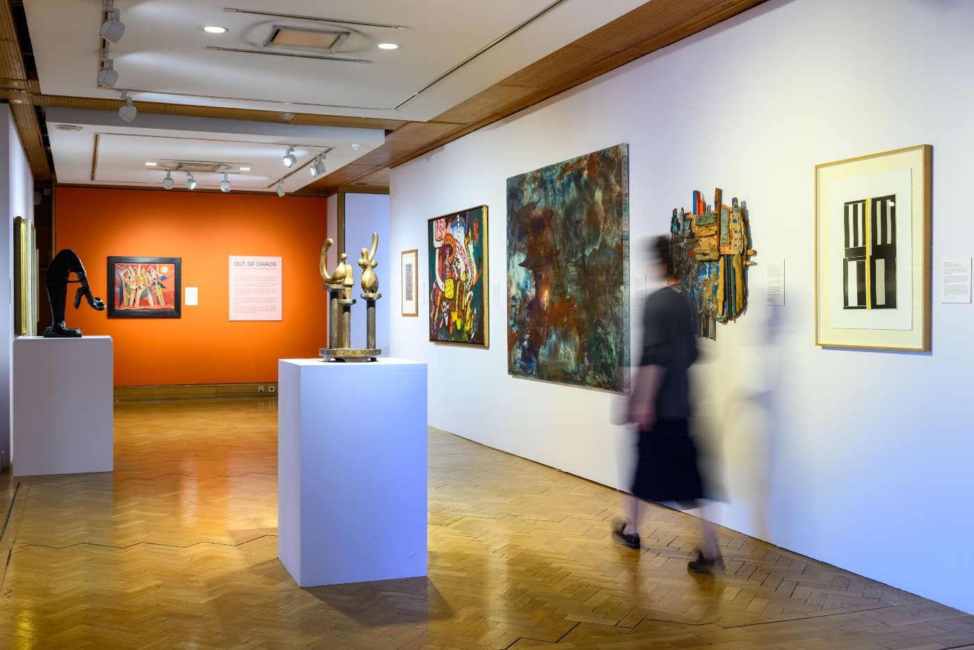 A woman strolls through an art gallery in Edinburgh with large paintings on display on the walls and two sculptures on display on plinths.