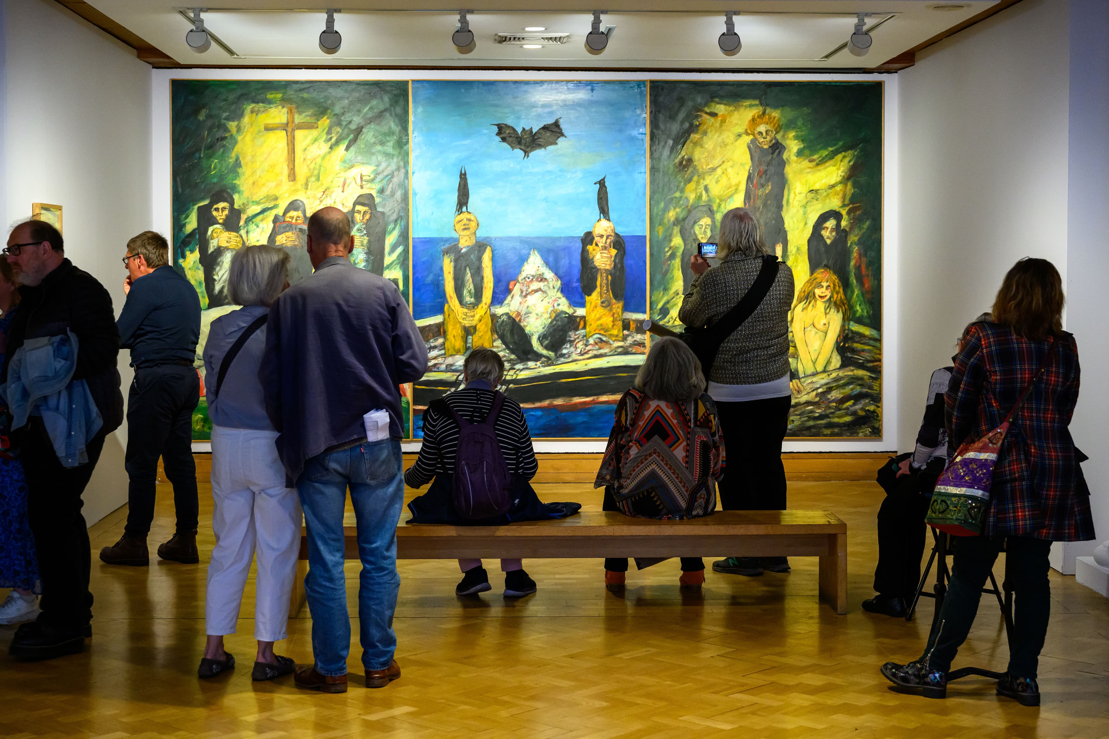 Art gallery-goers explore an art exhibit, intently looking at the paintings showcased on the gallery walls.