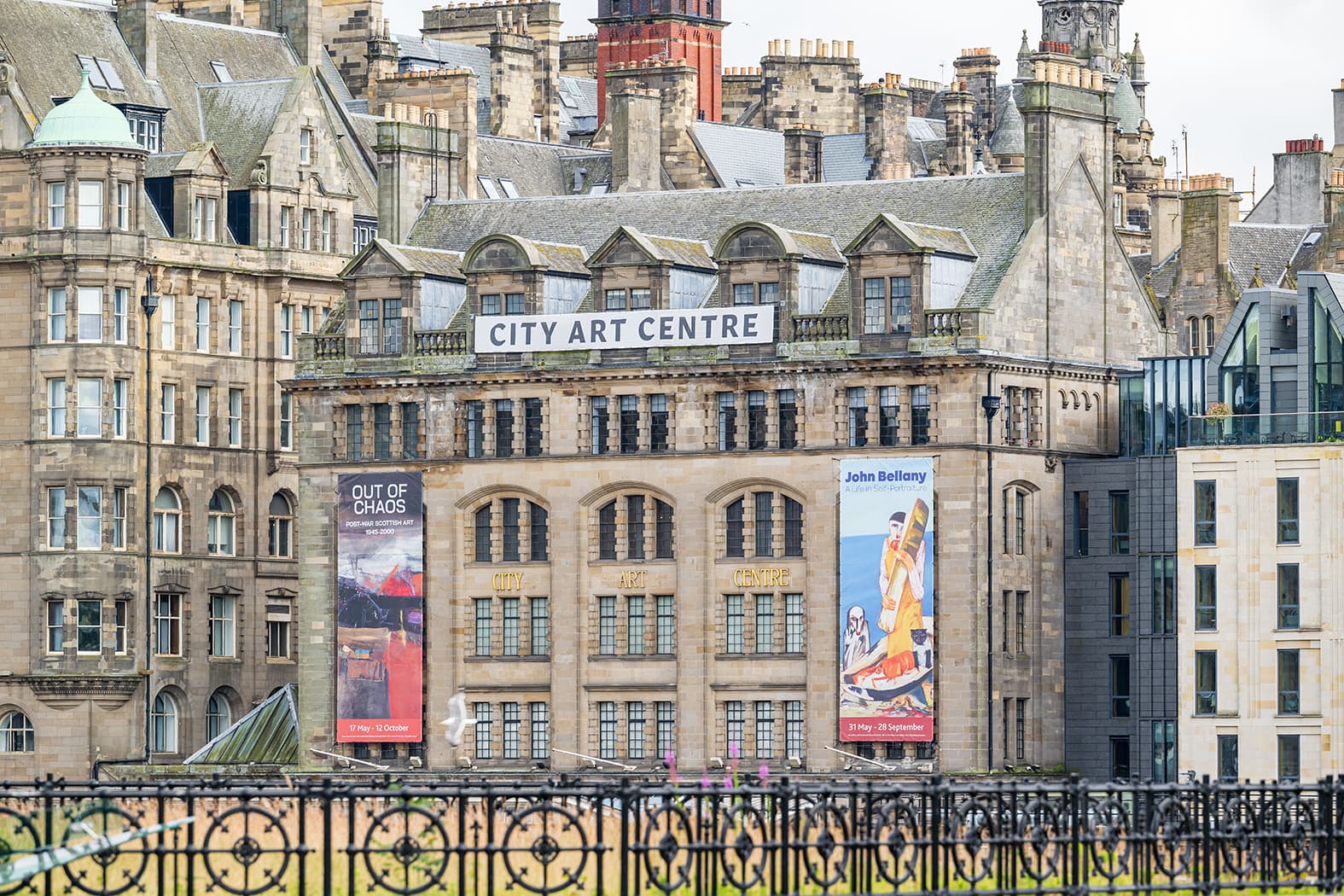 A large building featuring numerous windows, showcasing a modern architectural design. Two large banners hang down from the top windows showing exhibitions that are on in the gallery