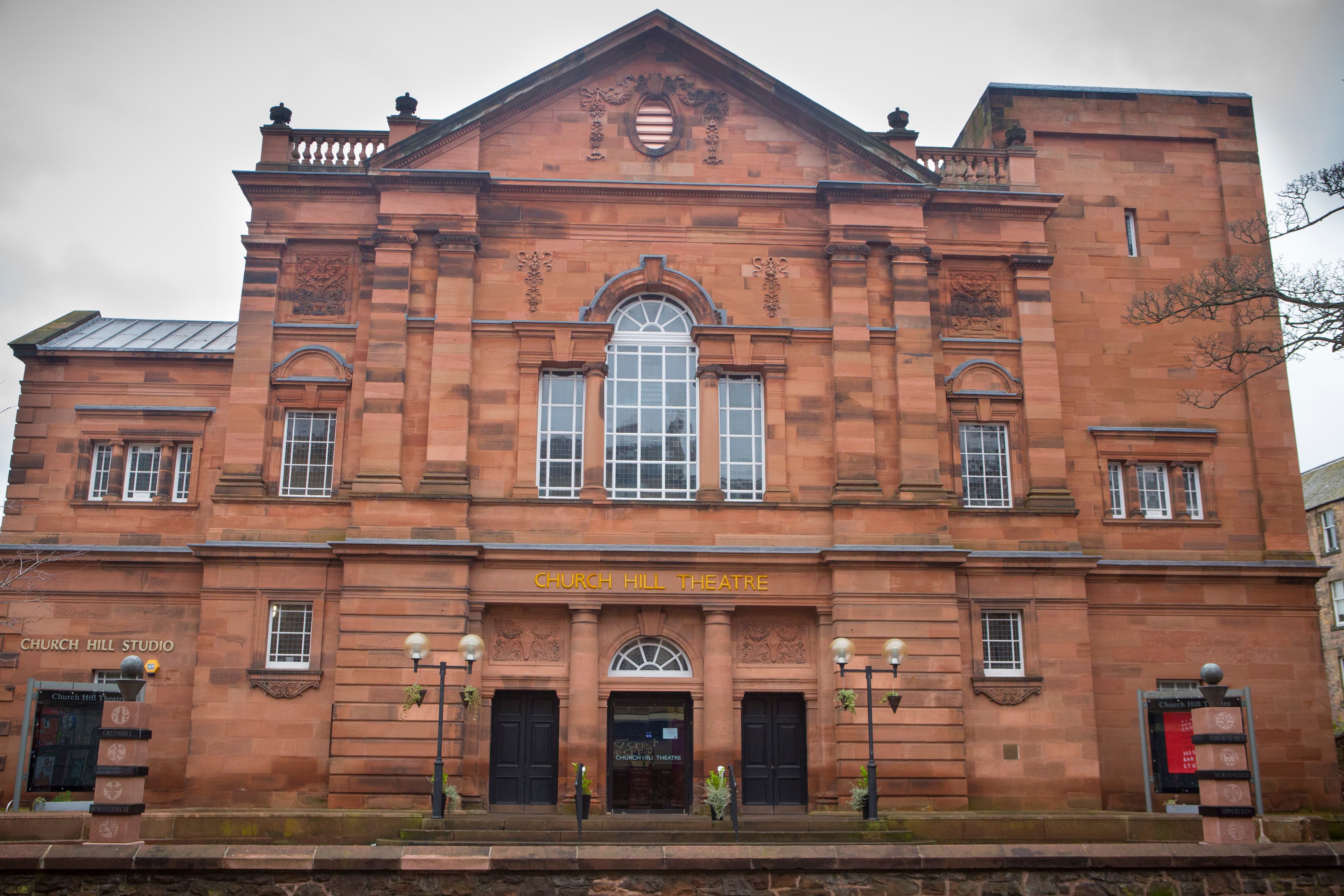 A large red brick building featuring a prominent elevation with an arch window against a clear sky.