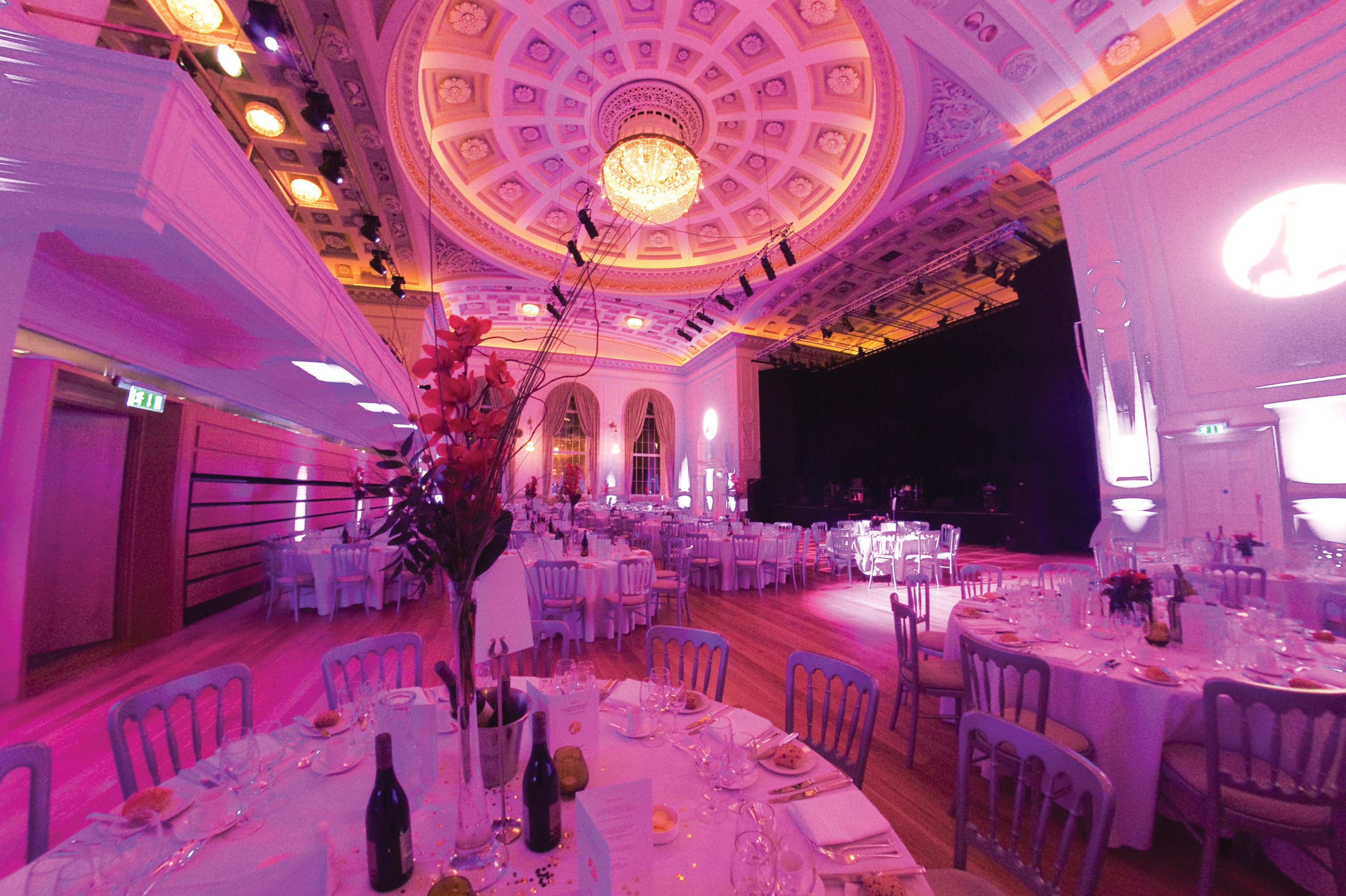 A large room bathed in purple light, showcasing multiple tables set up for an event or gathering.