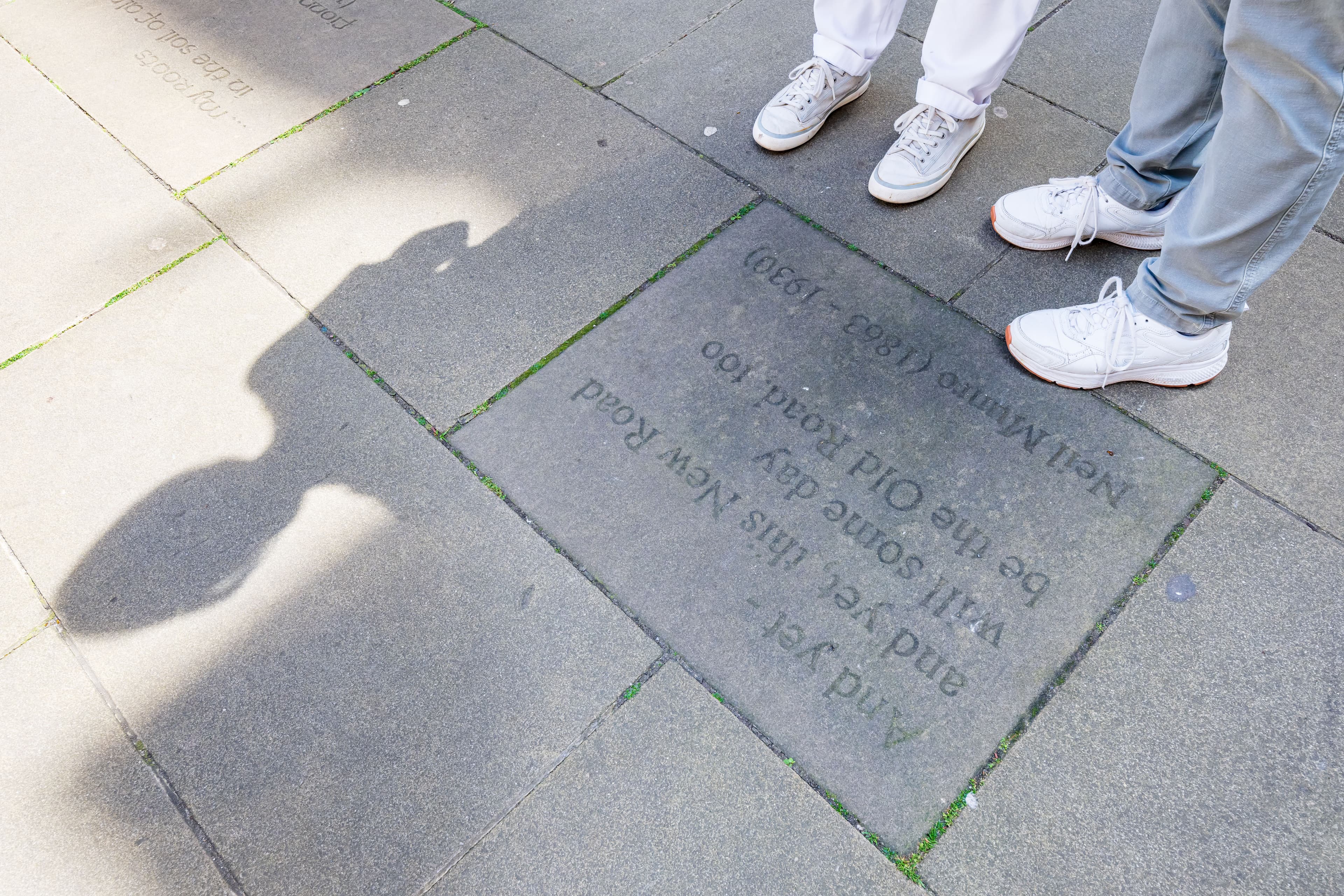 A man and a woman stand together on the pavement. The courtyard has engraved slabs under foot.