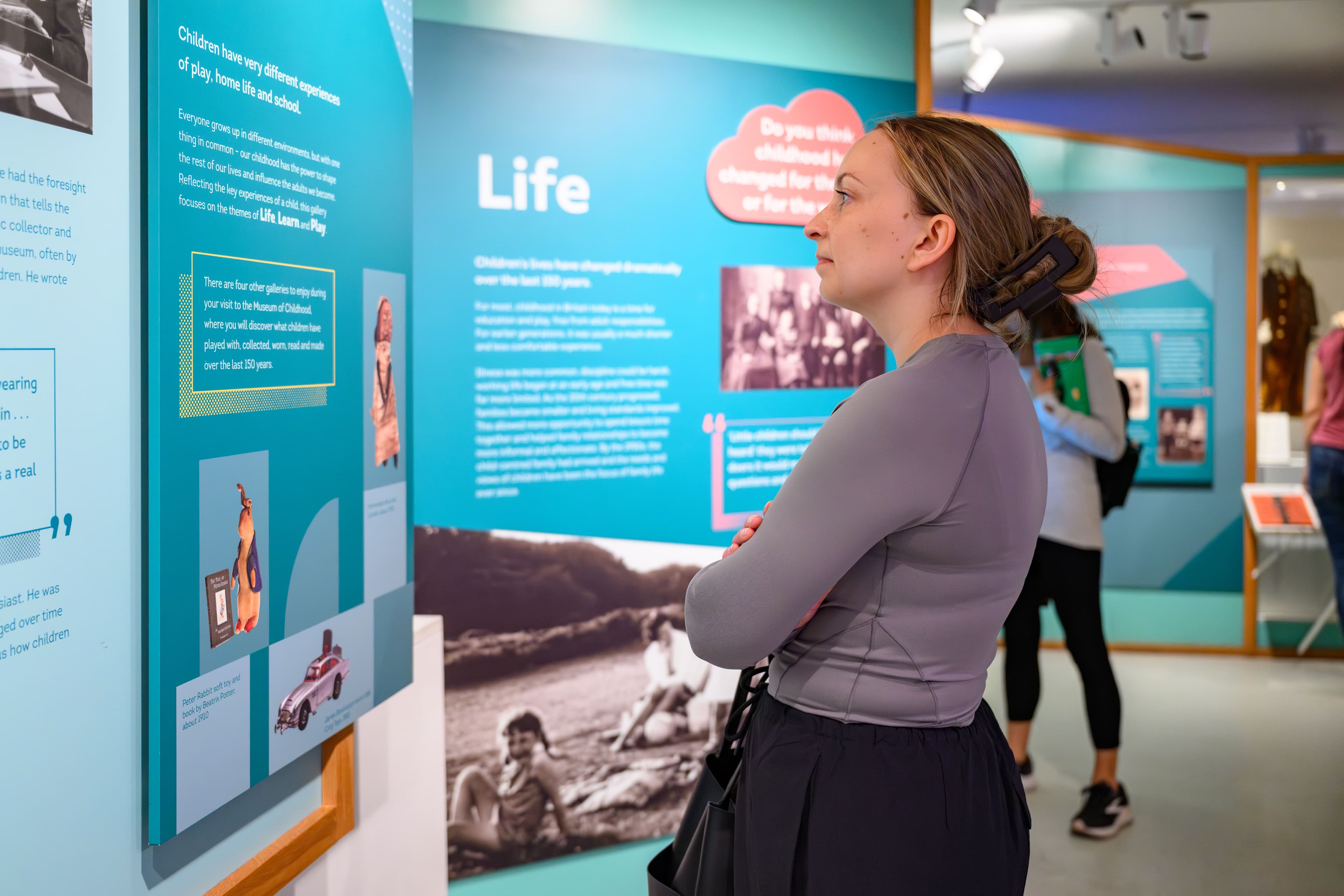 A woman visitor to a museum gazes thoughtfully at a display featuring information about life and childhood.