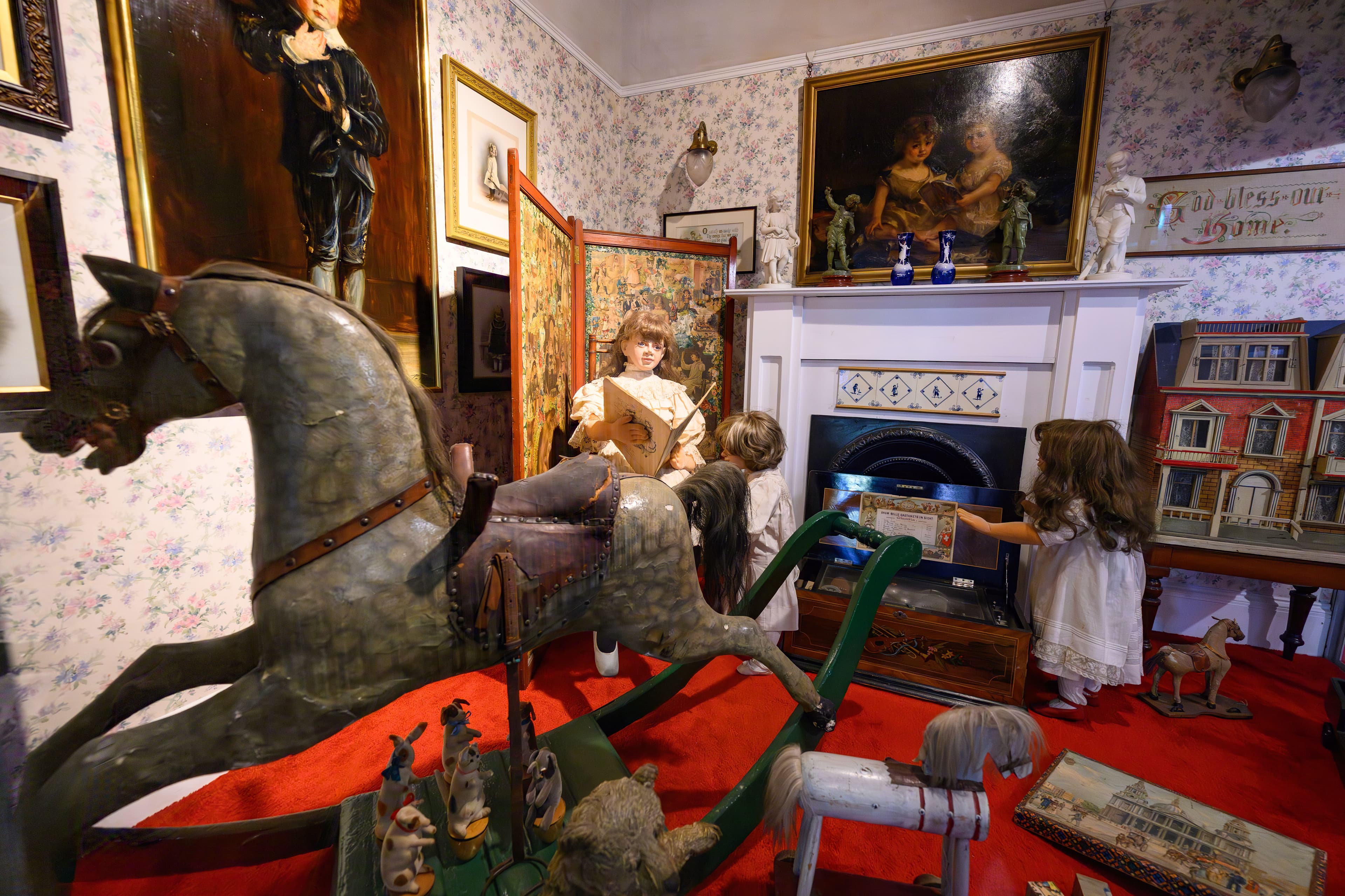 A cozy room featuring girls playing with books and toys including a wooden rocking horse, surrounded by colorful toys and soft lighting.