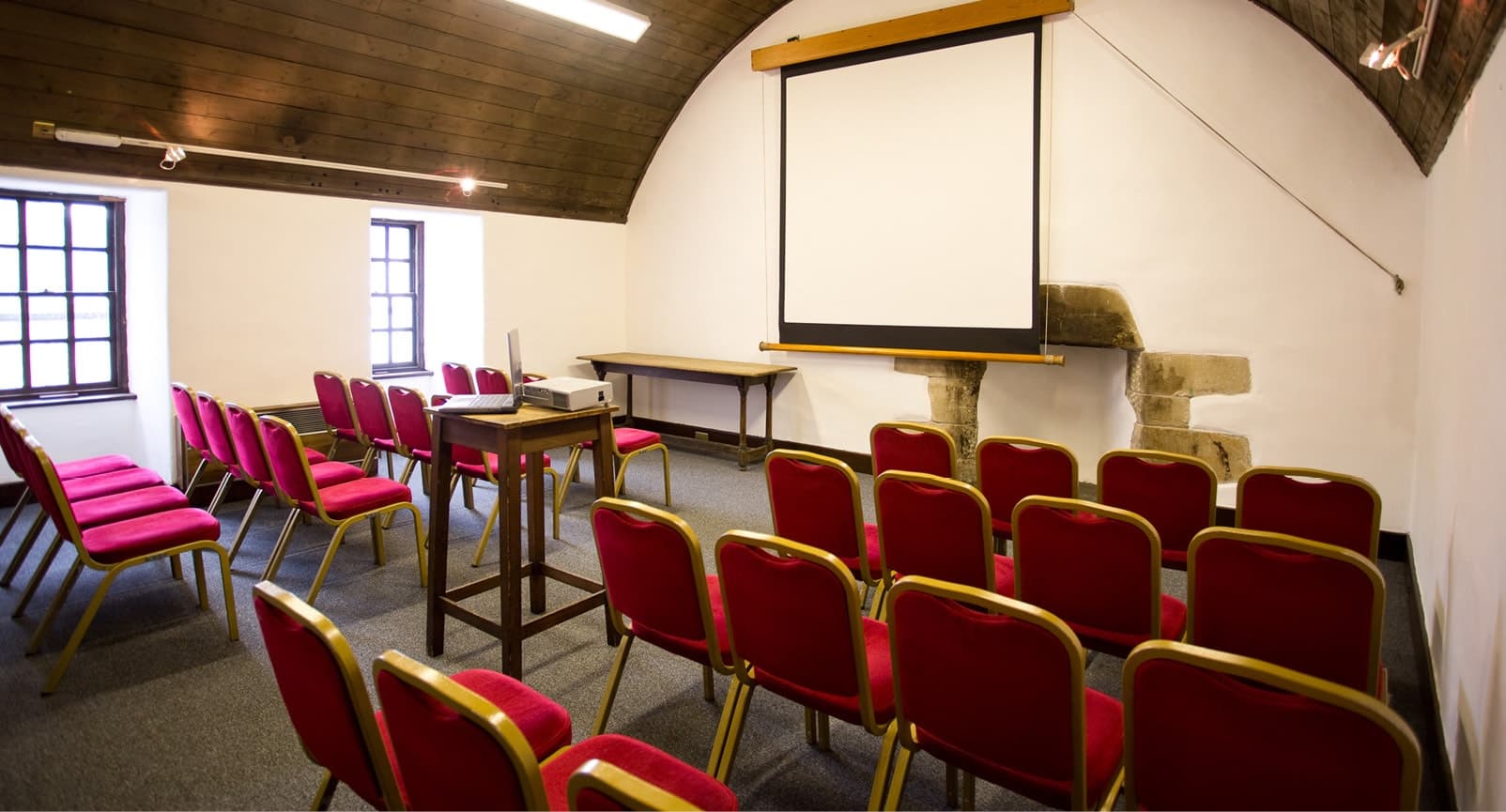 A conference room equipped with red chairs and a projector screen, ready for meetings and presentations.
