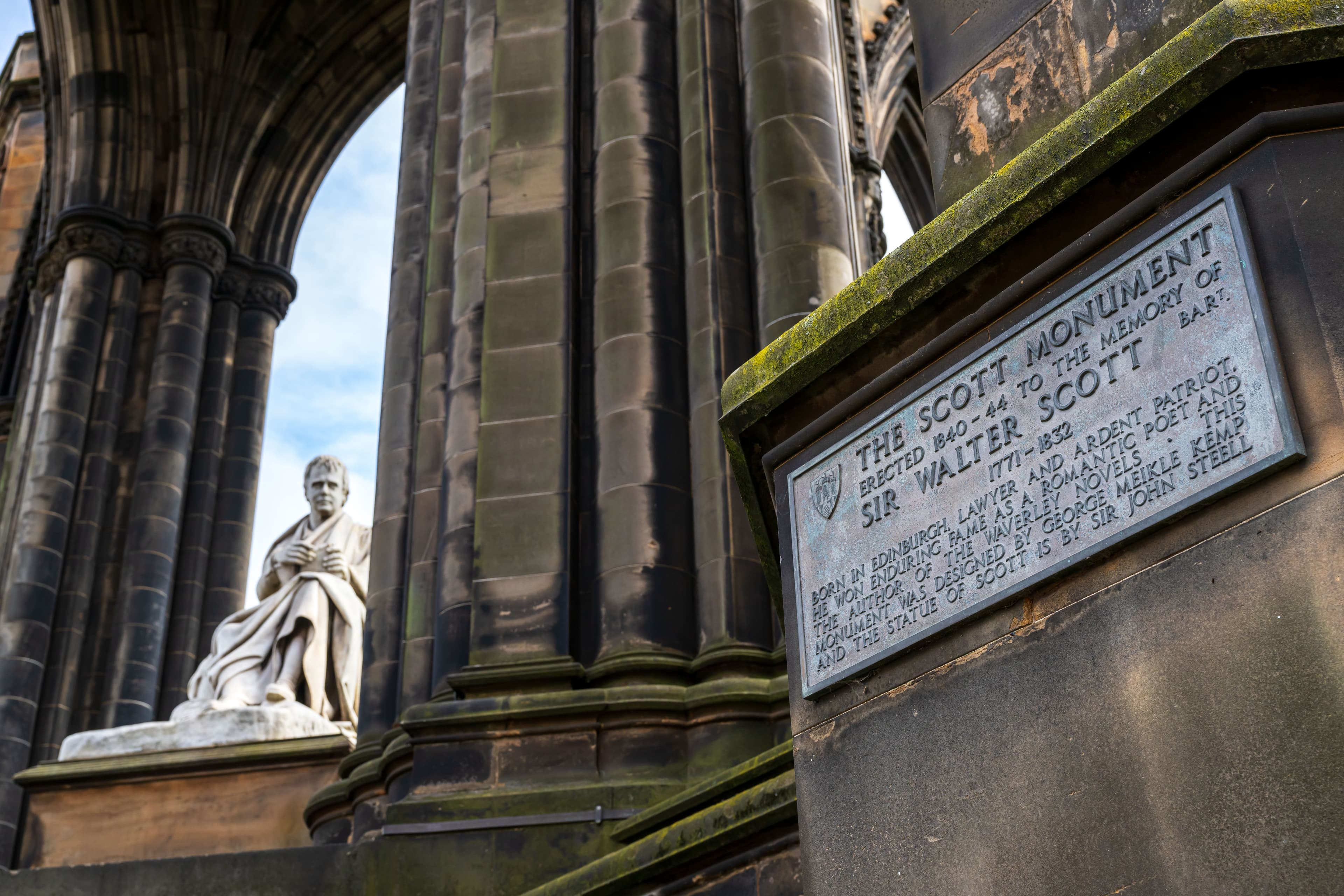 A statue depicting a marble statue sitting under pillars , accompanied by a plaque describing who the statue is.