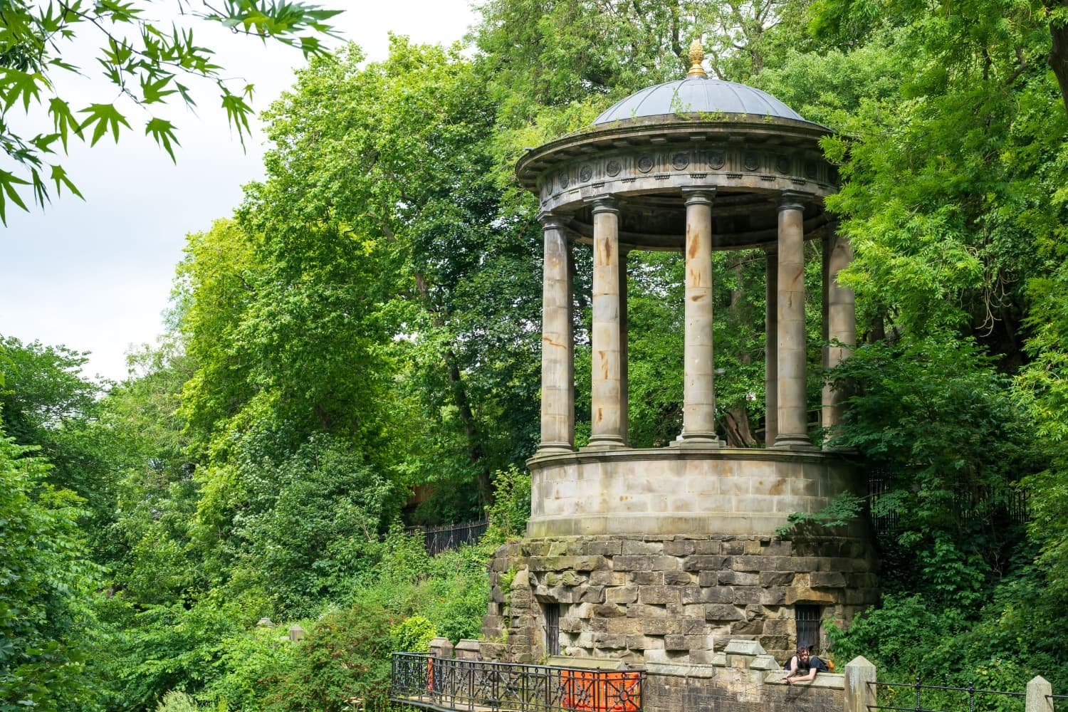 St Bernard's Well, a large stone structure, situated on the Water of Leith in Edinburgh surrounded by green trees.