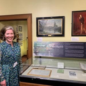 A volunteer stands beside a display case in a museum.