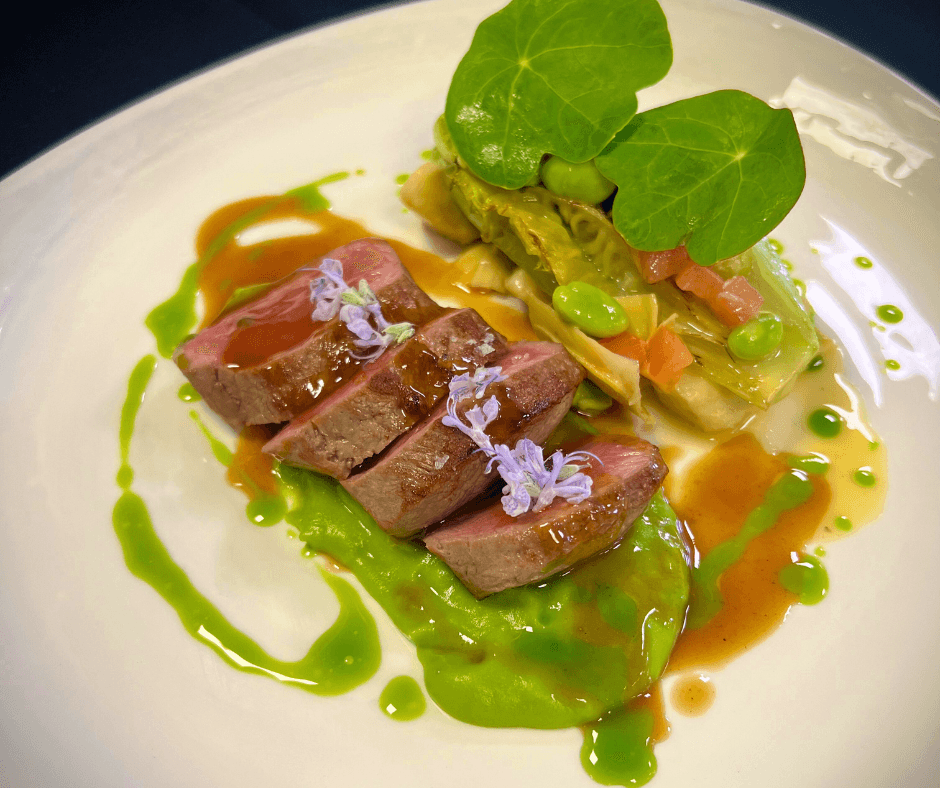 A white plate featuring a cooked steak drizzled with vibrant green sauce.