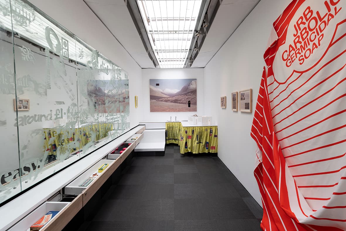 Inside the bus. White walls with artworks mounted onto them. Roof lights