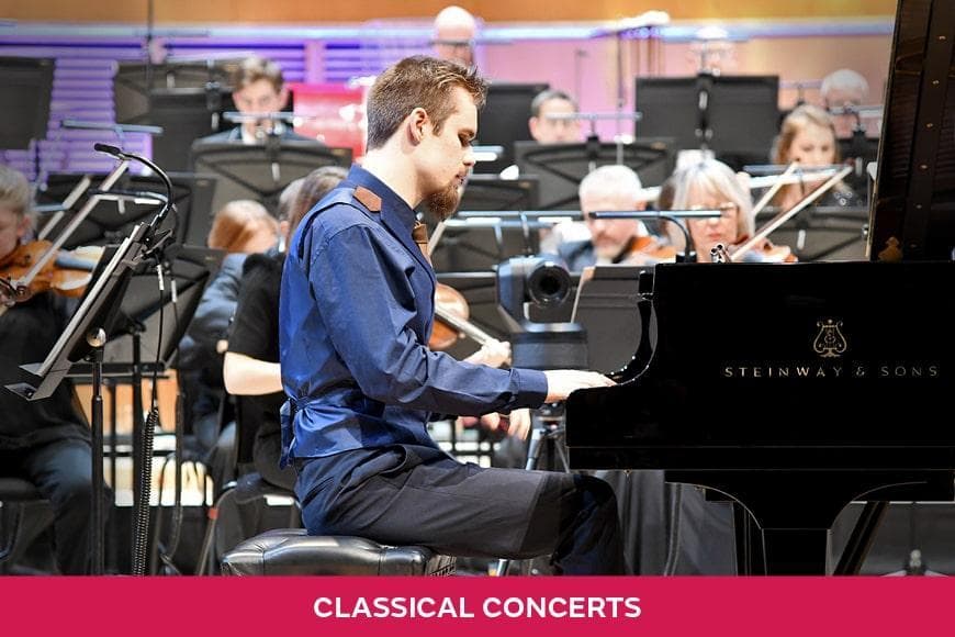 Ethan Loch sitting on stage playing the piano with an orchestra