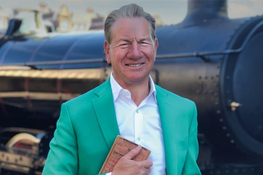 A headshot of Michael Portillo stood in front of a steam train smiling
