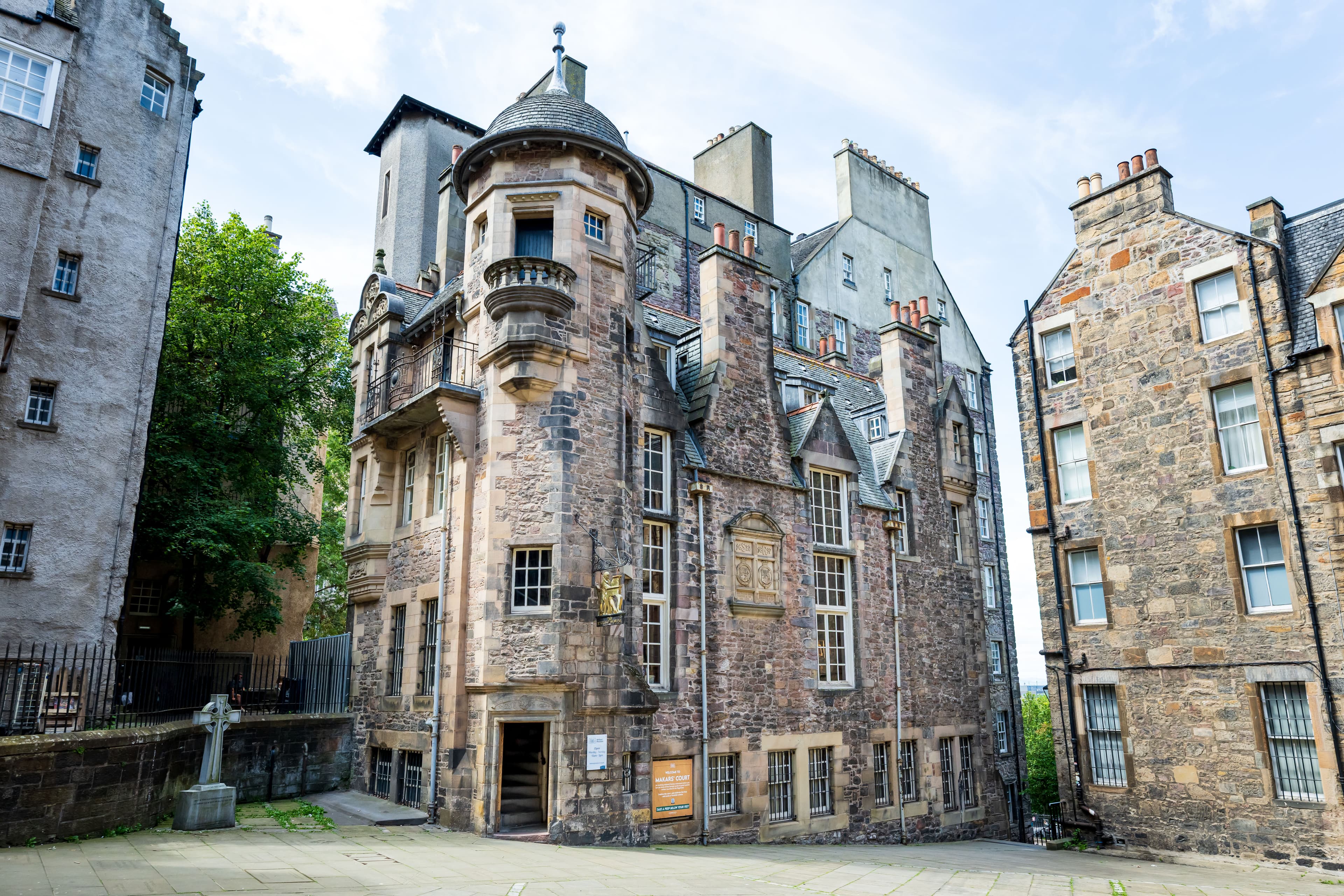 An imposing building highlighted by a turret with small windows, showcasing architectural detail sitting in a courtyard.