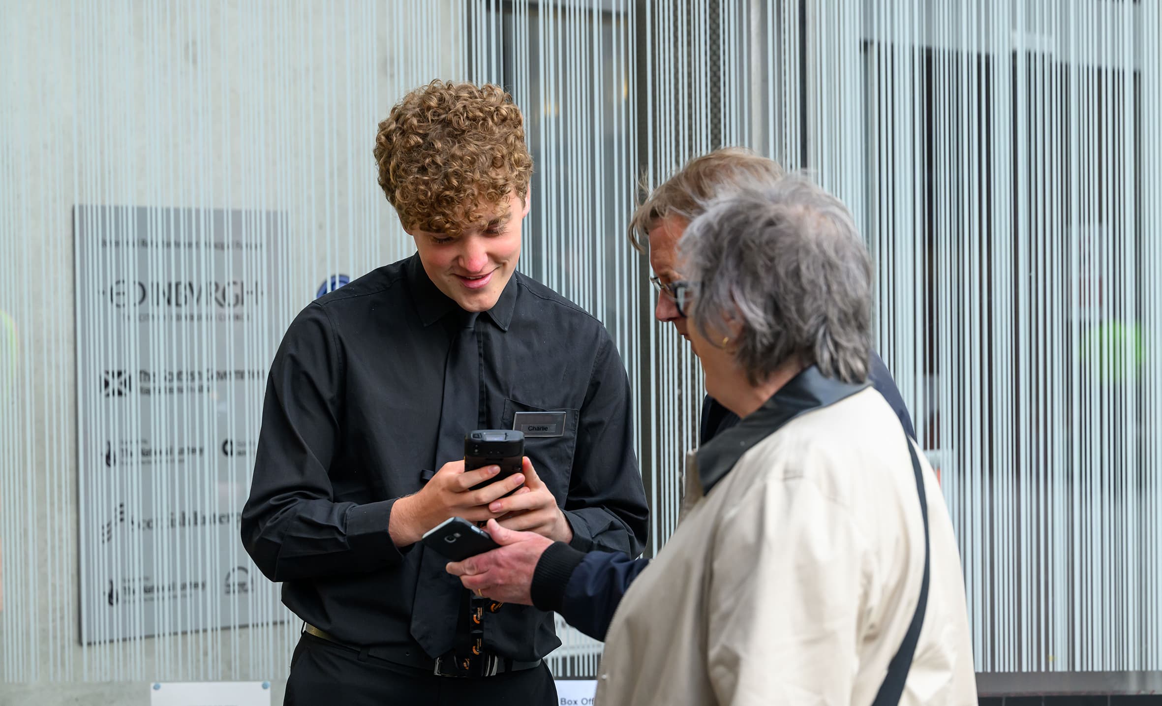 A Usher Hall staff member in a black shirt engages in conversation with two customers about tickets.