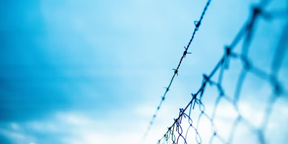 Prison fence and barbed wire against blue sky